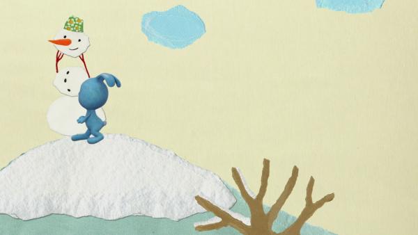 Kikaninchen steht neben einem Schneemann auf einem Berg.