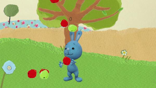Kikaninchen jongliert mit Äpfeln vor einem Apfelbaum.