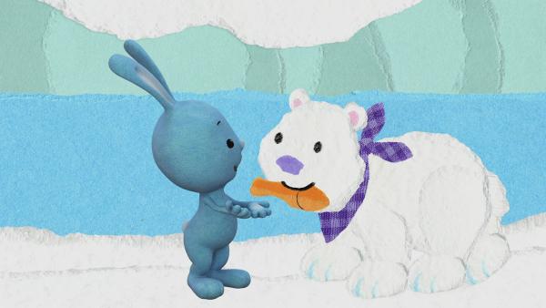 KiKANiNCHEN spricht mit einem kleinen Eisbären mit lila Halstuch und einem Fisch im Maul.