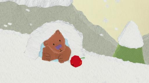 Ein Bär schaut aus einer Höhle. Davor liegt ein roter Apfel.