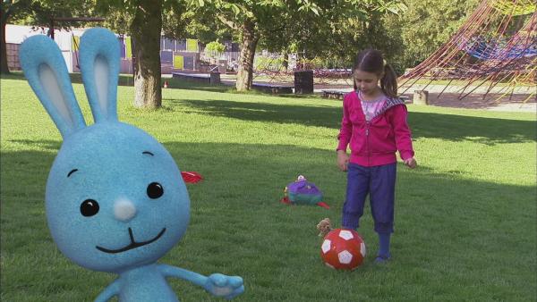 KiKANiNCHEN spielt mit einem kleinen Mädchen Fußball.