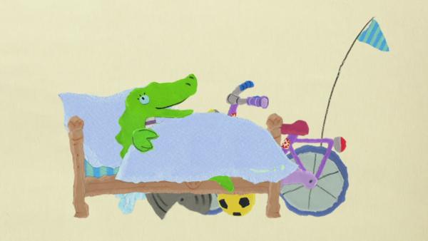 Ein Krokodil liegt im Bett, daneben steht ein Fahrrad