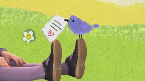 Der Vogelpostbote sitzt mit einem Brief im Schnabel auf den Füßen von Ida. 