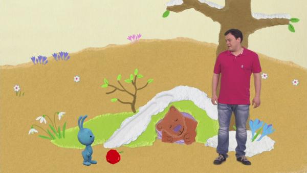 Kikaninchen und Christian stehen vor einer Höhle, in der ein Bär schläft.