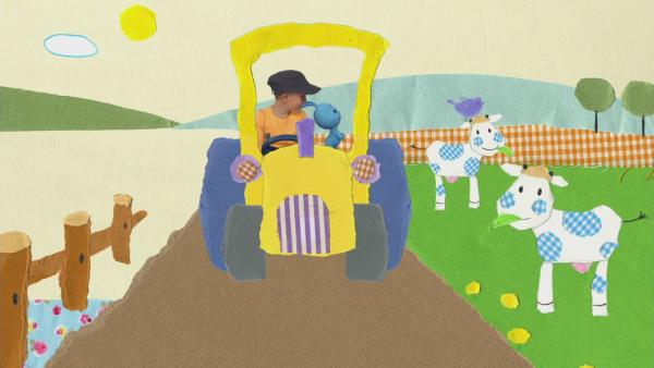 Kikaninchen und Ian fahren auf einem Traktor an einer Wiese mit Kühen vorbei.