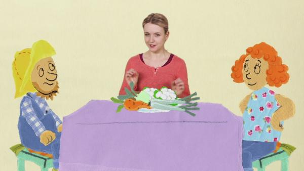 Anni, ein Fischer und eine Frau sitzen an einem Tisch mit Gemüse.