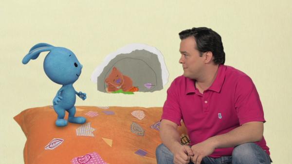Christian und Kikaninchen sizen auf einer Decke, in einer Höhle ein schlafende Bär