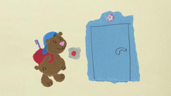 Ein Bär mit einem Rucksack steht vor einer blauen Tür.