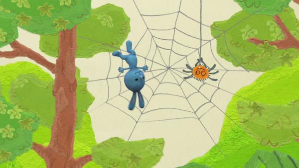KiKANINCHEN hängt kopfüber in einem Spinnennetz und lächelt eine kleine orangene Spinne an
