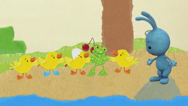 Kikaninchen, Entenküken und Frosch stehen Hand in Hand unter einem Kirschbaum. 