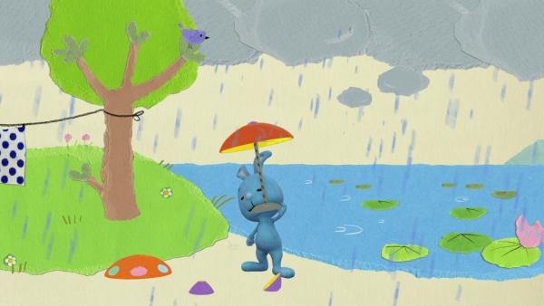 Kikaninchen steht mit einem Regenschirm im Regen am See.