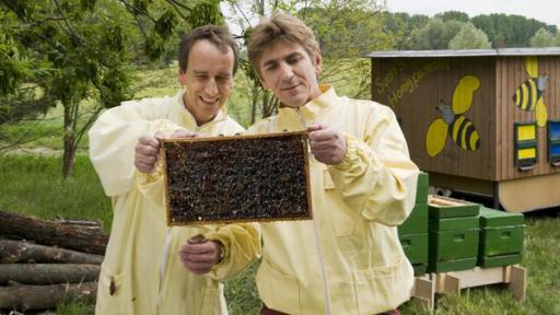 Fritz Fuchs steht vor einem Bienenwagen. Er trägt eine gelbe Regenjacke und seine rote Hose. 