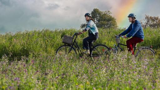 6. Regenbogen | Rechte: ZDF Fritz und Yasemin fahren mit dem Fahrrad durch Wiesen - im Hintergrund ist ein Regenbogen am Himmel zu sehen
