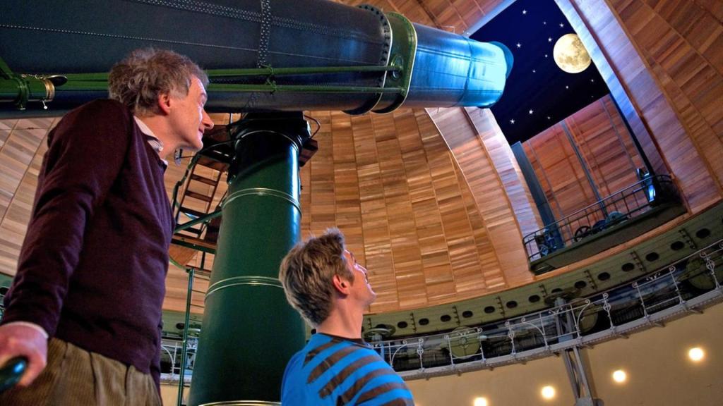 Fritz Fuchs steht mit einem Mitarbeiter des Observatoriums neben einem riesigen Teleskop und betrachtet den Mond.