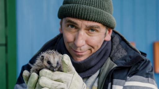 Fritz steht vor dem Bauwagen und hält einen Igel in den Händen