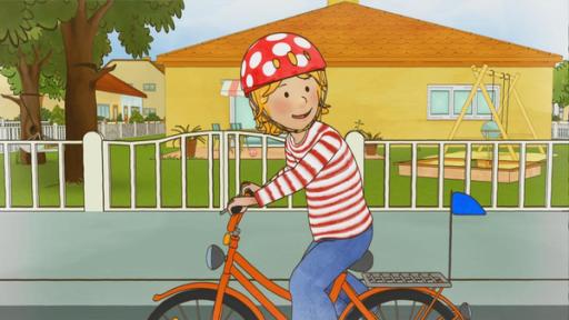 Conni sitzt mit Helm auf ihrem Fahrrad und übt den Schulterblick.