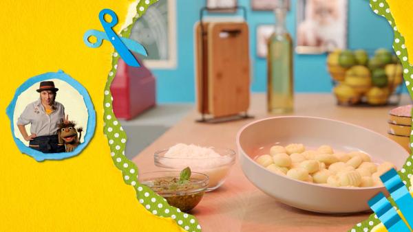 Selbstgemachte Gnocchi auf einem tiefen Teller, daneben steht geriebener Parmesan und Pest auf dem Tisch.