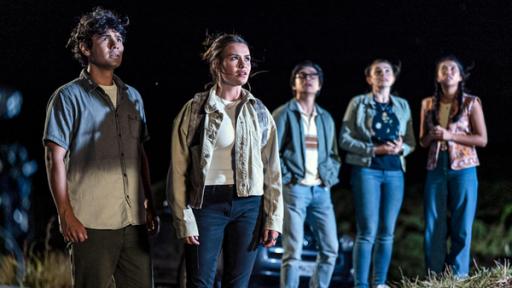 Der Fluch | Rechte: © Libertine Pictures Limited & Slim Film + Television Limited Dan (links), Issie (2.v.l.), Caleb (Mitte), Natasha (2.v.r.) und Caroline (rechts) stehen am Strand und blicken erstaunt in den Abendhimmel.
