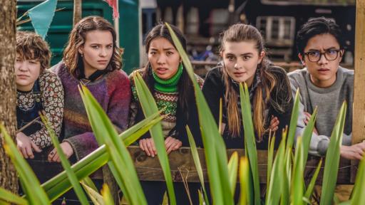 Mysteriöse Vorahnungen | Rechte: © Libertine Pictures Limited & Slim Film + Television Limited Draußen auf einem Fest hocken Stella (links), Issie (2.v.l.), Caroline (Mitte), Natascha (2.v.r.) und Caleb (rechts) nebeneinander und schauen erwartungsvoll über eine grüne Pflanze nach vorn.