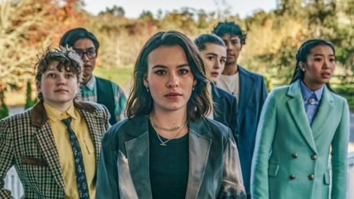 Rettungsaktion mit Folgen | Rechte: © Libertine Pictures Limited & Slim Film + Television Limited Issie (Mite), Stella (Mitte links), Natascha (Mitte hinten), Caroline (rechts), Caleb (hinten links) und Dan (hinten rechts) stehen als Gruppe mit angespannt fragenden Gesichtern auf einem Treppenaufgang an dem seitlich weiße Holzgeländer hochführen. Im Hintergrund sieht man Bäume.