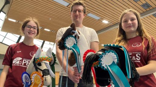 Hobby Horsing – Reiten auf dem Steckenpferd | Rechte: WDR | tvision Robert steht zwischen Rebecca und Melina in einer Turnhalle. Alle drei halten ein Steckenpferd in ihren Händen.