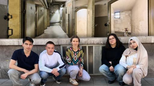Holocaust – Was hat das mit uns zu tun? | Rechte: WDR/tvision Reporterin Jana hockt zusammen mit vier Jugendlichen auf dem Boden vor einer Hauswand. Über ihnen ist ein Foto von Gefängniszellen projiziert, das aus dem NS-Dokumentationszentrum Kölns stammt.