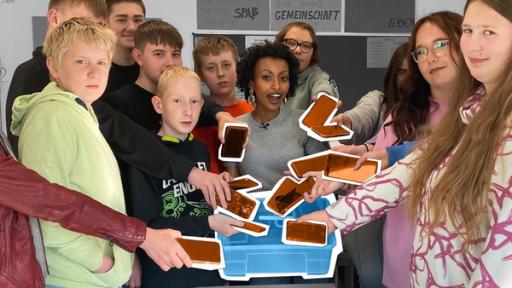 Leben ohne Handy - Das Smartphone-Experiment | Rechte: WDR | tvision Reporterin Luam steht im Klassenzimmer und hält eine Kiste. Um sie herum stehen Schülerinnen und Schüler, die ihre Smartphones in die Kiste legen.
