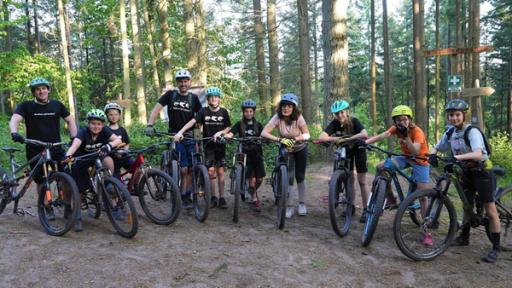 Mountainbiking - Umweltfreundlich über Stock und Stein | Rechte: WDR | tvision Gruppenfoto: Sieben Kinder, zwei Erwachsene und Reporterin Tessniem stehen mit Helmen und Mountainbikes im Wald und lächeln in die Kamera.