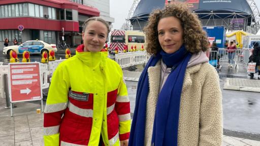 Helferin Johanne und Reporterin Gesa stehen vor der Kölner Anlaufstelle für Geflüchtete aus der Ukraine am Hauptbahnhof.