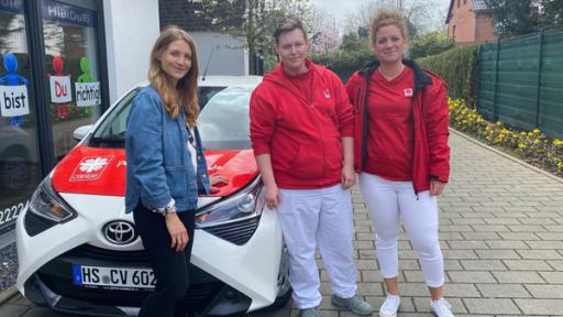 Reporterin Jana steht mit Luca und Denise vor einem Auto.