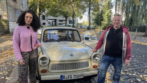Die Helden des Mauerfalls | Rechte: WDR/tvision Reporterin Tessniem und Zeitzeuge Michael Heinisch-Kirch stehen neben einem Trabi in Berlin.