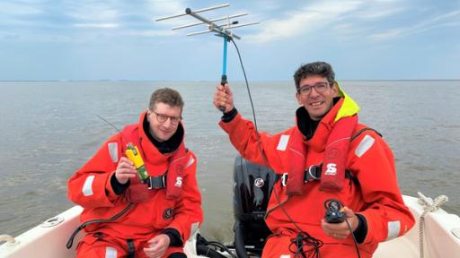 Unterwasserlärm – Warum es im Meer zu laut ist | Rechte: WDR/tvision Reporter Robert und der Unterwasserlärm-Forscher Joseph „Jeff“ Schnitzler sitzen in einem Boot. Robert hält einen Sender in der Hand und Jeff eine Antenne.