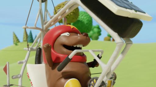 Nö Nös Kumpel Tüftel trägt seinen roten Helm und seine gelben Gummstifel. Er sitzt in einem selbstgebauten weißen Fahrrad mit Überrollbügel und streckt erfreut die rechte Faust in die Höhe. Im Hintergrund ist eine grüne Landschaft.