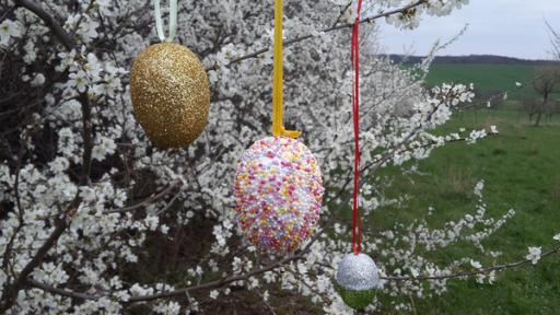 glitzernde Ostereier an einer blühenden Hecke