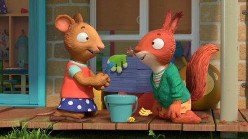 Der Zaubertrank | Rechte: © Magic Light Pictures LTD 2023 Tagsüber auf der Holzveranda des Hauses spielen Posy, die Maus und Jamila das Eichhörnchen - sie brauen einen Zaubertrank. Beide knien vor einem Eimer und überlegen, welche Zutaten sie mixen können. Posy hält eine blaue Feder in der Hand und blickt zu Jamila, die zustimmend lächelt.