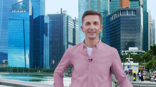 Moderator Eric Mayer steht vor der Skyline von Singapur an einem Geländer vor einem Fluss und lacht in die Kamera.