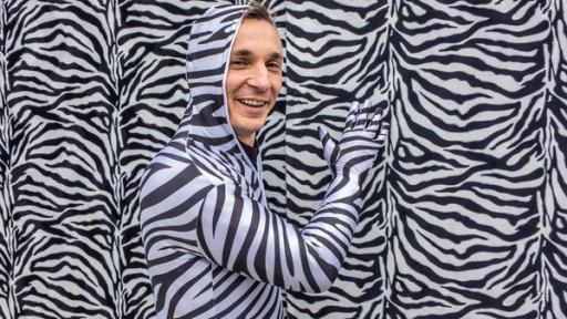 PUR+ - Teaser - Tarnung | Rechte: Imago PUR+ Sendung Tarnung: Moderator Eric Mayer steht in einem Ganzkörper-Kostüm im Zebralook vor einer Wand im Zebralook. Nur sein Gesicht trägt keine Zebrastreifen und ist ungeschminkt.