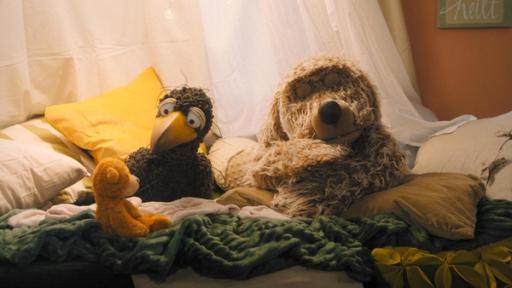 Land unter Mär | Rechte: ZDF Rabe Rudi hockt in der gemütlichen Kuschelecke. Er schaut einen orangefarbenen Teddybären an. Rechts daneben schläft Hund Buffo.