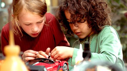 zwei Kinder beugen sich über ein rotes Spielzeugauto
