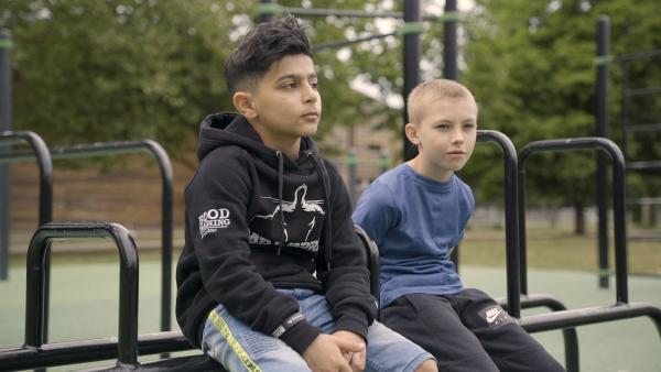 Bahzad (links) und Andriy (rechts) sitzend auf einer Trainingsstange. Im Hintergrund sieht man weitere Gerüststangen zum trainieren.