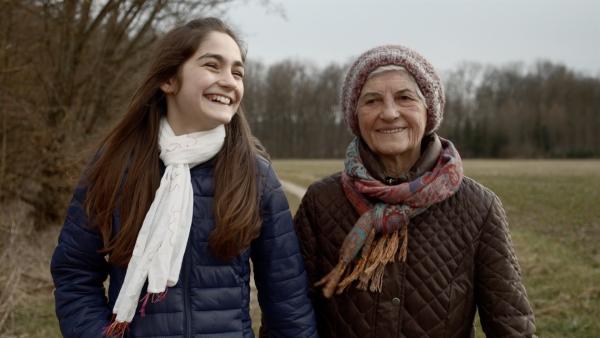 Noa geht mit ihrer Oma auf einem Feldweg spazieren.