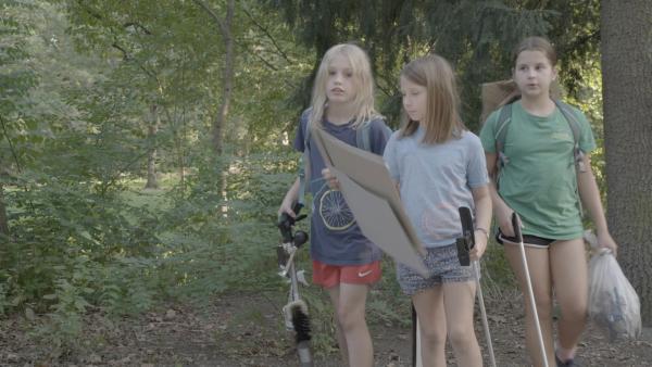 Eva (Mi.) und ihre Freundinnen Nordje und Emmy hängen Plakate im Park auf.