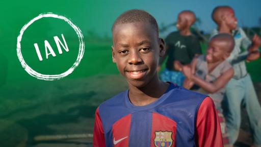 Foto von Ian aus Uganda. Er trägt ein Trikot des Fussballverein FC Barcelona. Im Hintergrund tanzt eine Gruppe von Kindern.