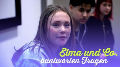 Elma (Rolle Frida) sitzt neben Einstein-Darstellern. Bildtext: Elma und Co. beantworten Fragen