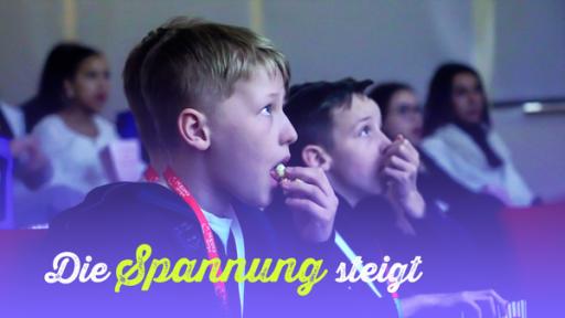 Zwei Jungs schauen spannend auf eine Kinoleinwand und essen Popcorn. Bildtext: Die Spannung steigt.