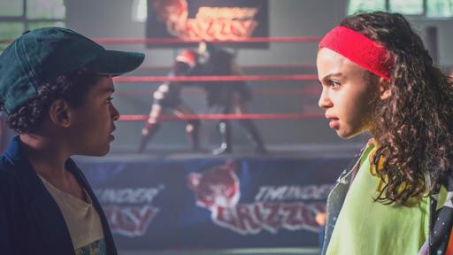 Zwei Teenager unterhalten sich vor einem Boxring im Hintergrund.