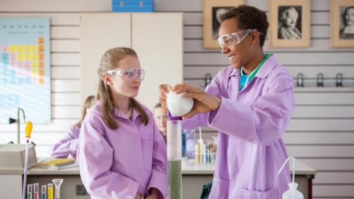 Zwei Schüler mit Schutzbrille und Kittel im Chemieunterricht.