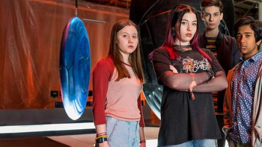 Silverpoint, Staffel 2 - Teaser - MT25 - Folge 01: Das Spiel beginnt | Rechte: © Zodiak Kids & Family Productions UK Ltd Von links nach rechts: Meg, Kaz, Louis und Glen stehen in einer Lagerhallen. Hinter ihnen sind drei sehr große so genannte Artefakte zu sehen. Sie leuchten in verschiedenen Farben und haben verschiedene geometrische Muster auf der Oberfläche. Alle schauen entschlossen in die Kamera. Kaz hat die Arme vor der Brust verschränkt.