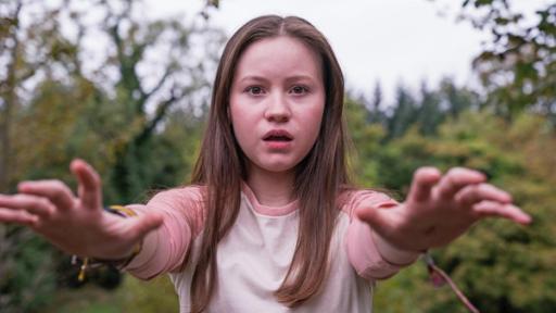 Silverpoint, Staffel 2, Folge 09: Mächtige Meg | Rechte: © Zodiak Kids & Family Productions UK Ltd Meg, gespielt von Katy Byrne , steht draußen vor Bäumen und Büschen. Der Wind weht ihr ins Gesicht und sie schaut angestrengt nach vorne. Ihr Blick sieht besorgt aus.