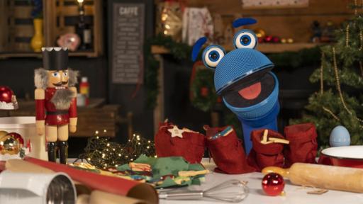 SingDing Weihnachtsplaylist | Rechte: ZDF Das SingDing schaut mit geneigtem Kopf und geöffnetem Mund lachend in die Kamera. Vor dem SingDing liegen auf einer Küchenarbeitsfläche durcheinander Backutensilien, Kekse und Weihnachtsdekoration sowie ein selbst gebastelter Adventskalender aus kleinen Stoffbeuteln. Im Hintergrund steht ein Weihnachtsbaum.